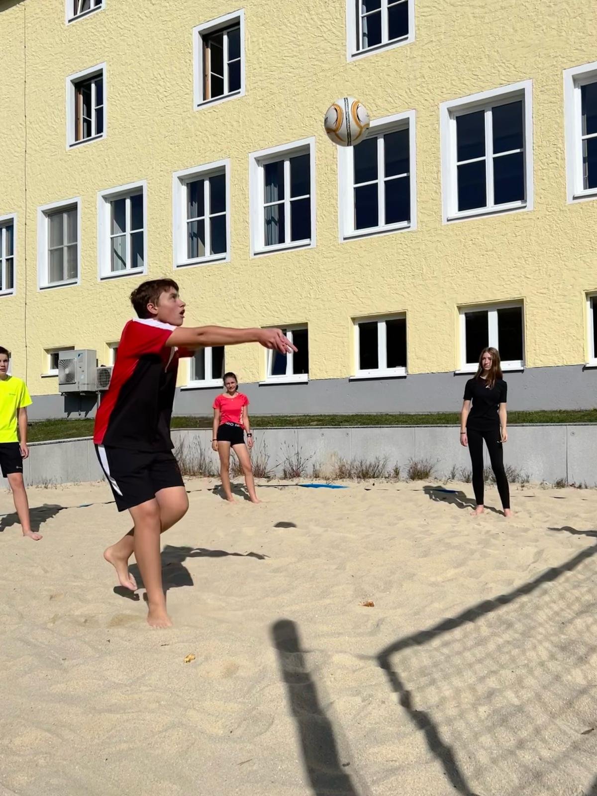 Schüler schießt den Ball über das Volleyballnetz, am Beachvolleyballplatz.